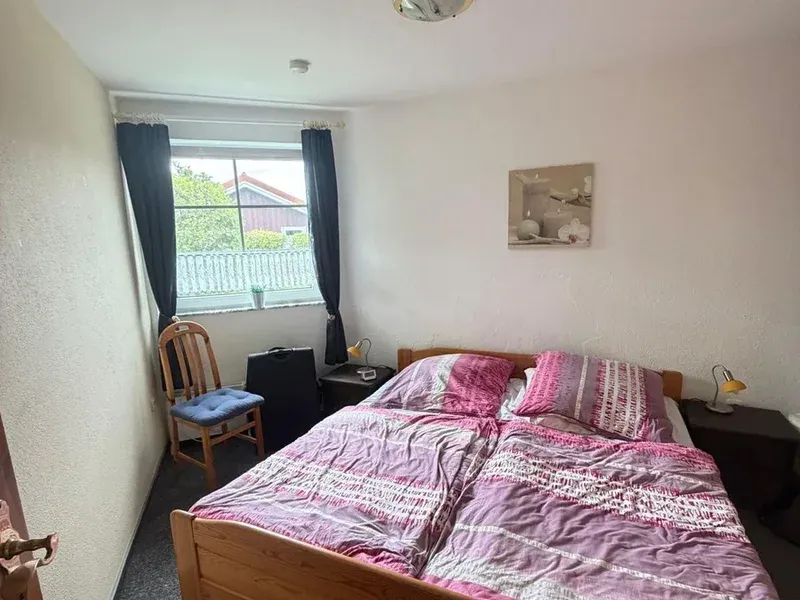 Schlafzimmer vor der Renovierung mit altem Holzbett, vergilbten Wänden und Teppichboden