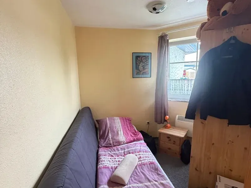 Kleines Zimmer vor der Renovierung mit altem Schlafsofa, gelben Wänden und Teppichboden